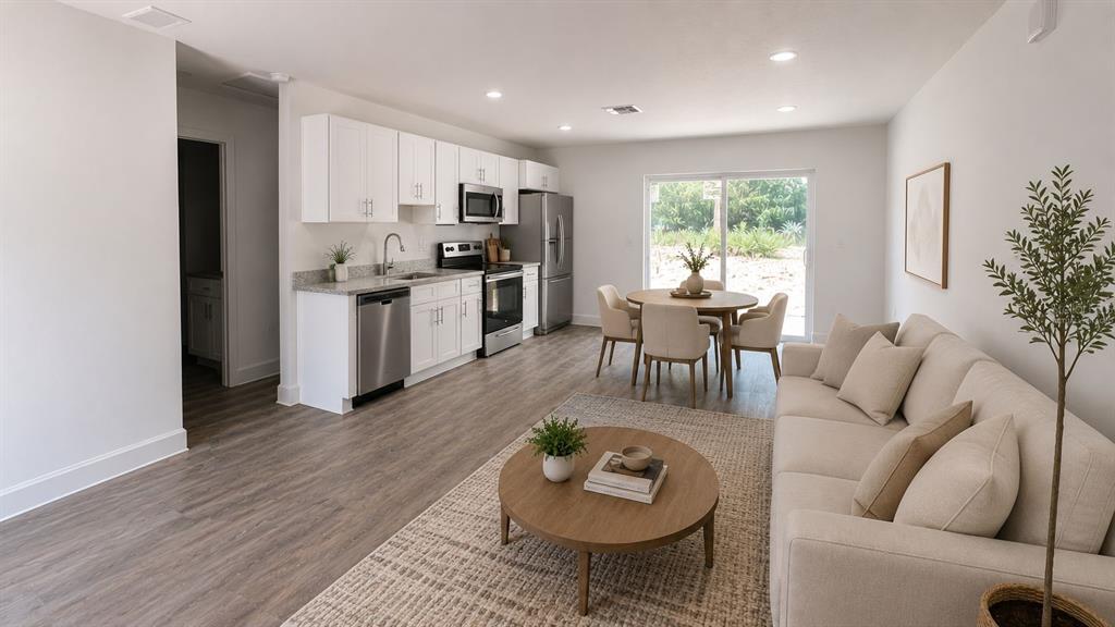 An open-concept kitchen, dining area, and living room feature white cabinetry, stainless appliances, and wood-look flooring — 423 WATER ROAD, OCALA, FL