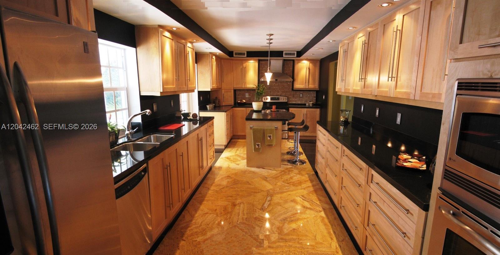 A kitchen features light wood cabinets, black countertops, and polished stone flooring — 7240 SW 119th St, Pinecrest FL 33156, PINECREST, FL