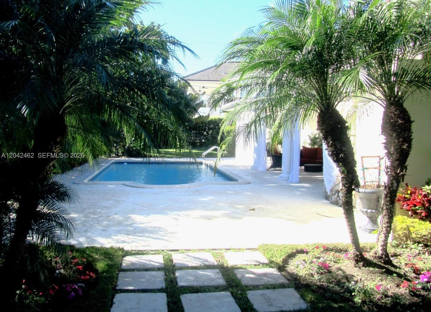A swimming pool sits on a stone patio surrounded by palm trees and landscaping — 7240 SW 119th St, Pinecrest FL 33156, PINECREST, FL