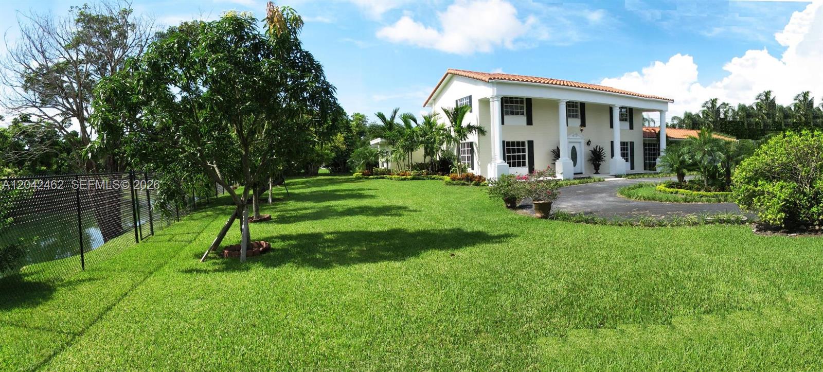 A two-story white house with a columned porch sits on a large, grassy lawn — 7240 SW 119th St, Pinecrest FL 33156, PINECREST, FL