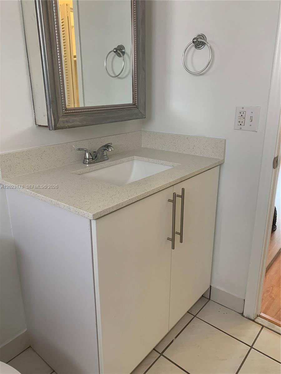 A bathroom vanity features a white cabinet, speckled countertop, undermount sink, and a framed mirror — 7703 Camino Real # 405, Miami FL 33143, MIAMI, FL
