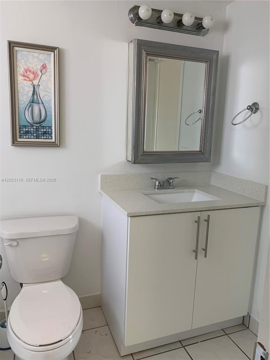 A bathroom features a white vanity with a quartz countertop, a mirror, and a toilet — 7703 Camino Real # 405, Miami FL 33143, MIAMI, FL