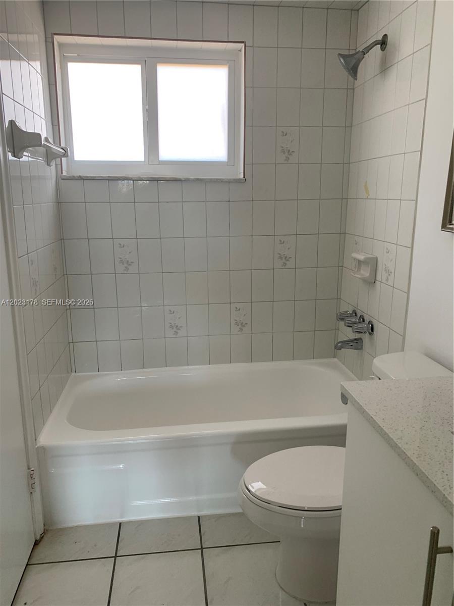 A bathroom features a white bathtub, a toilet, and white tiled walls with floral accents — 7703 Camino Real # 405, Miami FL 33143, MIAMI, FL