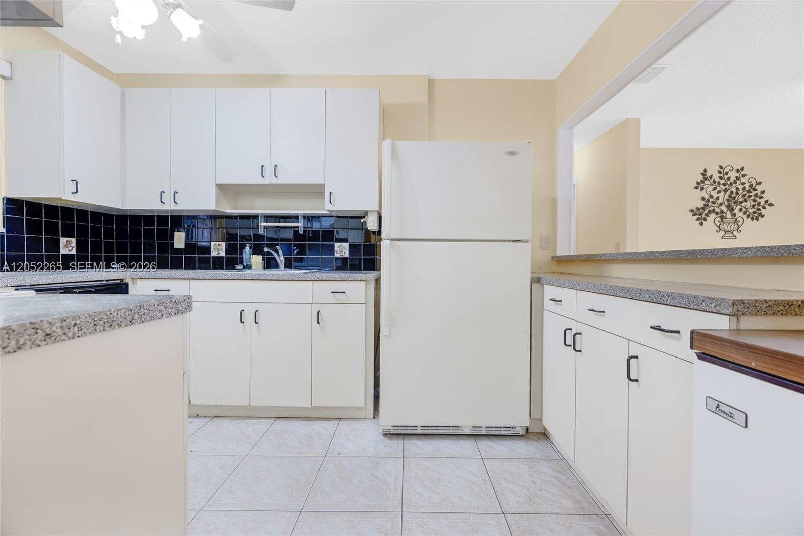A kitchen features white cabinets, black tile backsplash, a white refrigerator, and granite-look countertops — 16420 NE 5th Ave # 000, Miami FL 33162, MIAMI, FL
