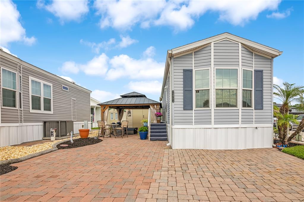 A paved patio sits between two manufactured homes with a gazebo and outdoor seating area — 2451 CITRUS TREE ROAD, CLERMONT, FL