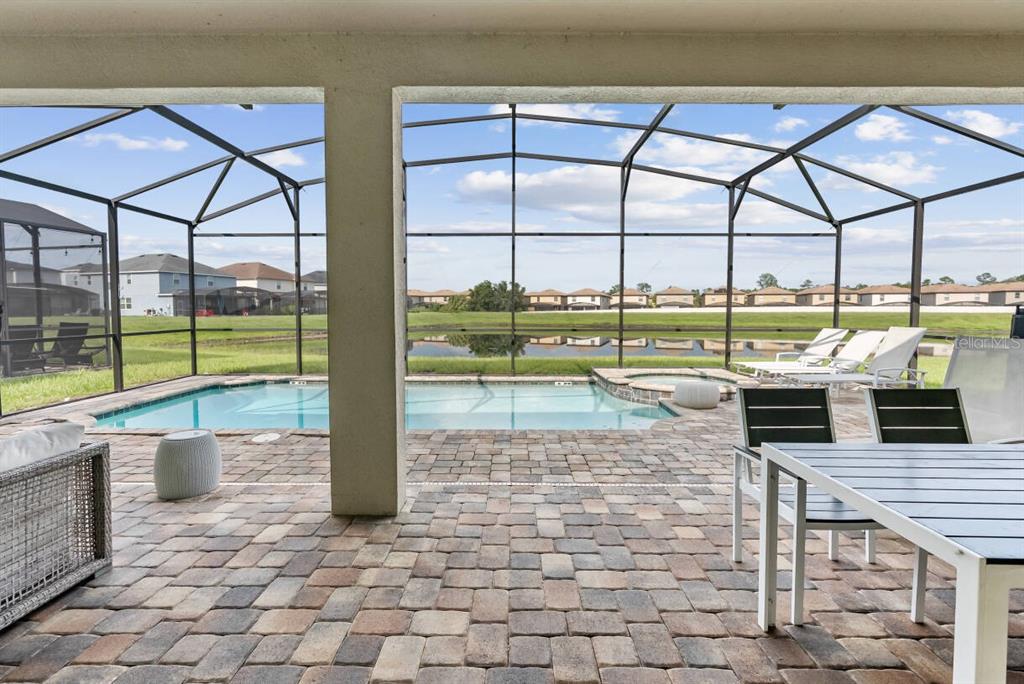 A screened-in patio features a paver deck, a swimming pool, and a view of a pond — 2145 FLEMING MIST PLACE, KISSIMMEE, FL