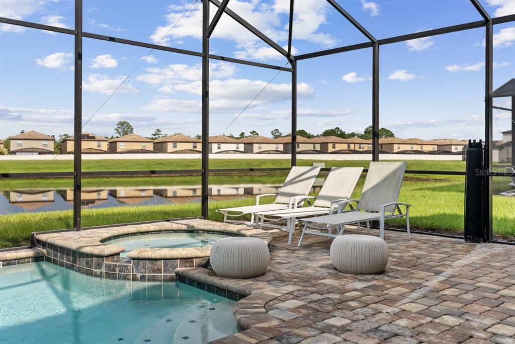 A screened-in pool patio features a hot tub, lounge chairs, and a view of water — 2145 FLEMING MIST PLACE, KISSIMMEE, FL