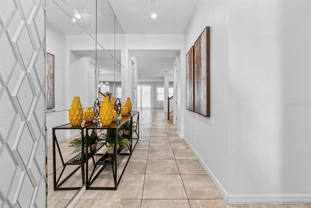 A tiled hallway features a mirrored wall, a black metal console table, and yellow vases — 2145 FLEMING MIST PLACE, KISSIMMEE, FL