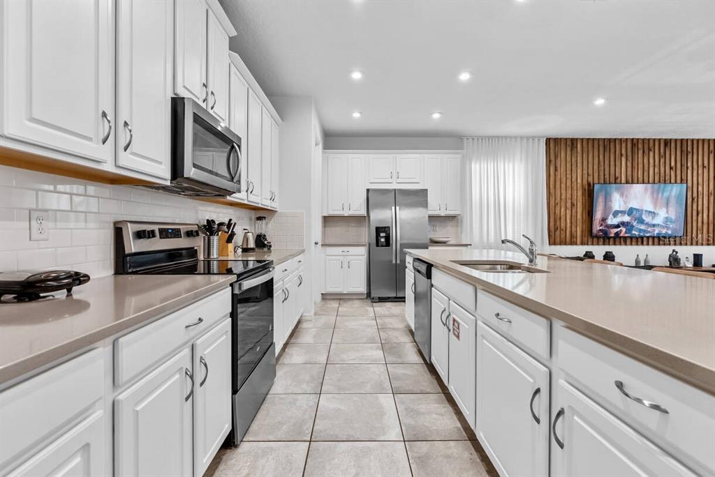 A modern kitchen features white cabinetry, stainless steel appliances, and a large central island — 2145 FLEMING MIST PLACE, KISSIMMEE, FL