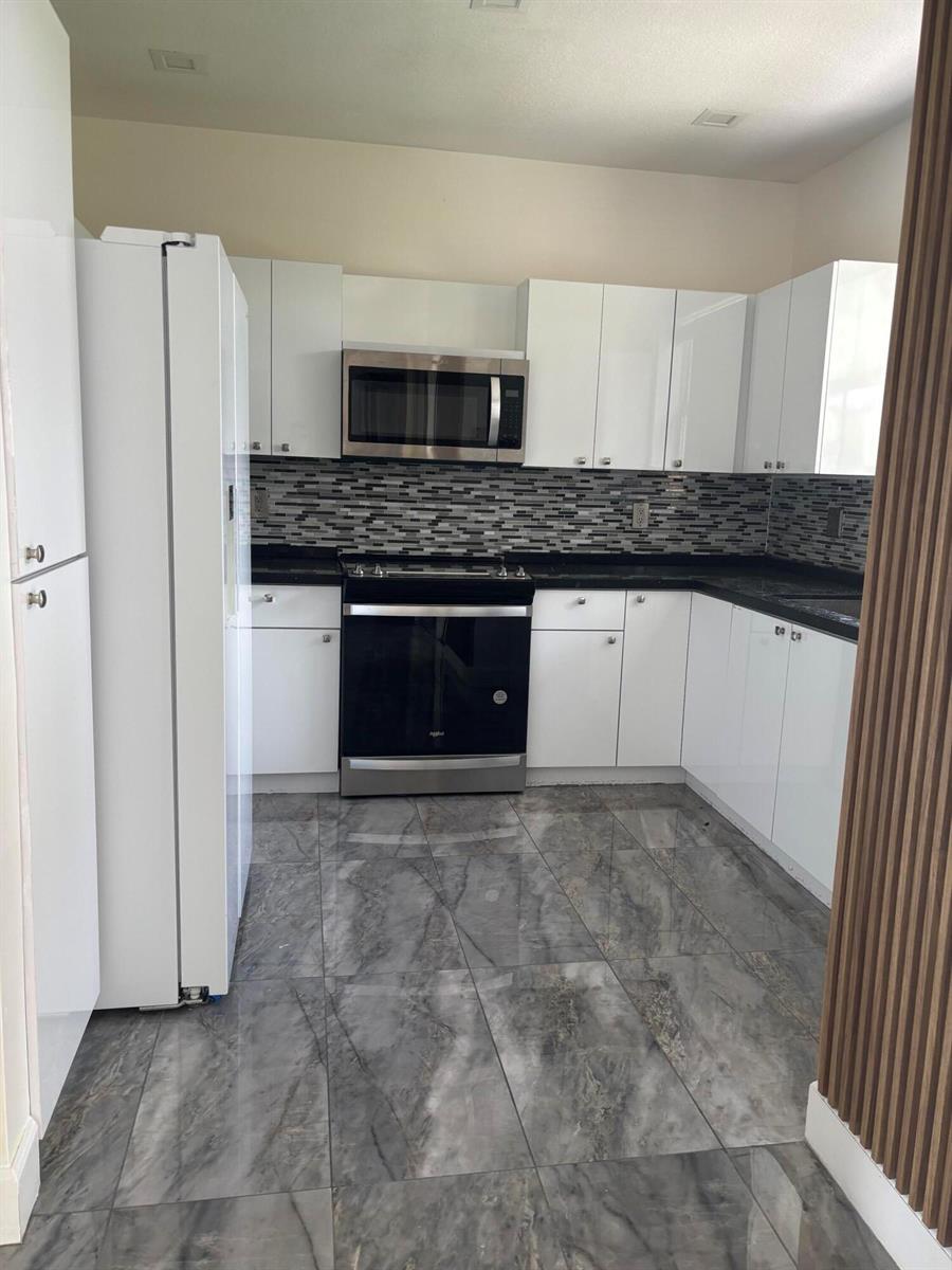 A kitchen features white cabinets, stainless steel appliances, a mosaic backsplash, and gray marble flooring — 254 Riverwalk Circle # 254, Sunrise FL 33326, SUNRISE, FL