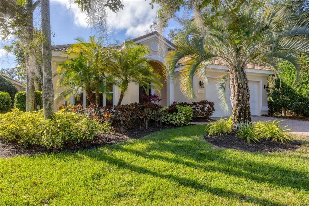 A single-story house with a tan stucco exterior, a tile roof, and a landscaped front yard — 8404 ABINGDON COURT, UNIVERSITY PARK, FL