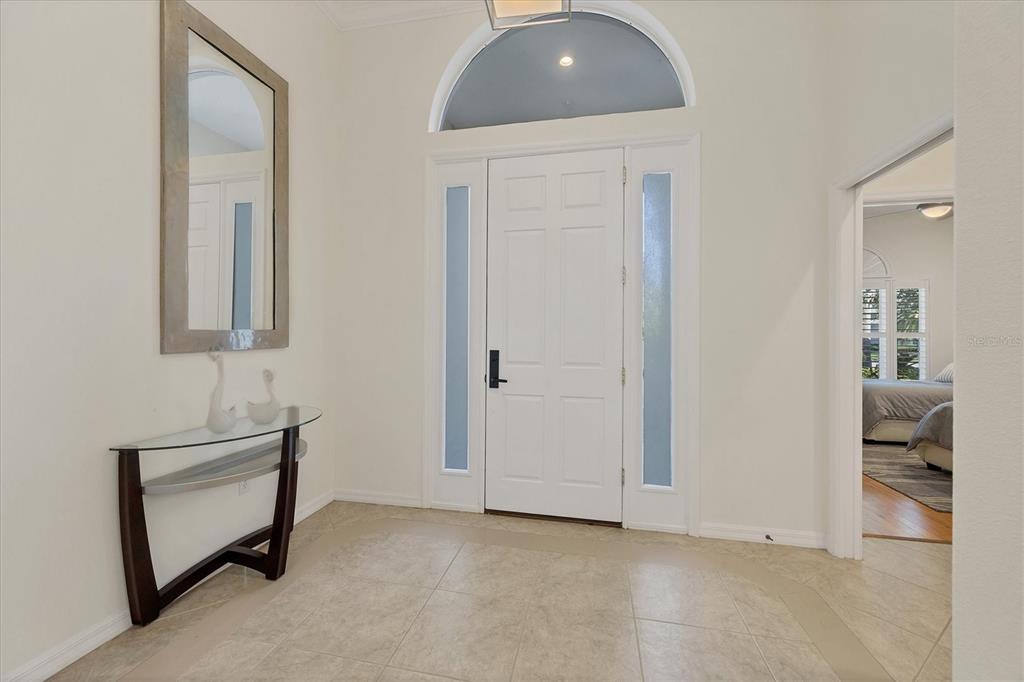 A bright entryway features a white front door with sidelights, a glass console table, and mirror — 8404 ABINGDON COURT, UNIVERSITY PARK, FL
