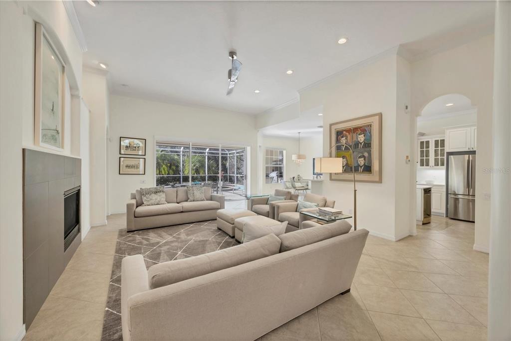 A living room features a fireplace, neutral sofas, tile flooring, and an open kitchen view — 8404 ABINGDON COURT, UNIVERSITY PARK, FL