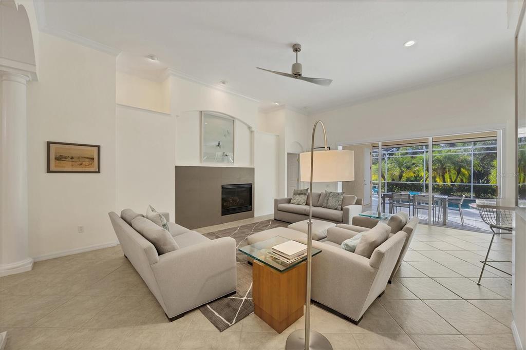 A living room with a fireplace, light-colored sofas, tile flooring, and a sliding glass door — 8404 ABINGDON COURT, UNIVERSITY PARK, FL