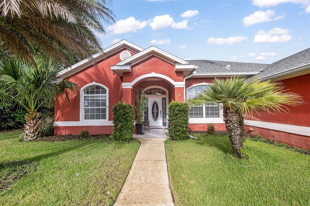 A red stucco house with a white-trimmed arched entryway and a concrete walkway — 7 FARVER LANE, PALM COAST, FL