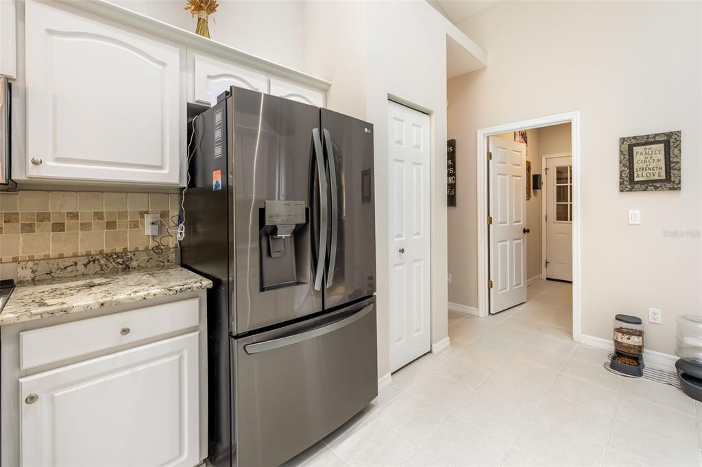 A kitchen features a stainless steel refrigerator, white cabinets, granite countertops, and tile flooring — 7 FARVER LANE, PALM COAST, FL
