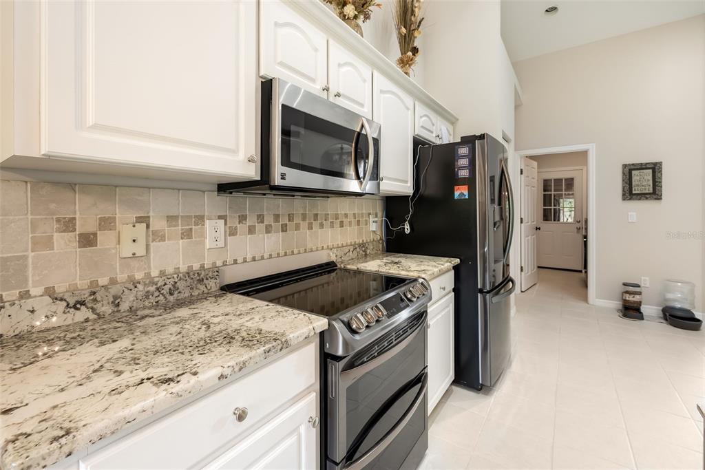 A kitchen featuring white cabinets, granite countertops, stainless steel appliances, and a tiled backsplash — 7 FARVER LANE, PALM COAST, FL