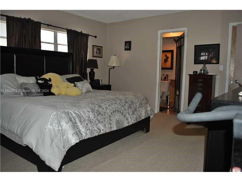 A bedroom features a large bed with patterned bedding, dark curtains, and an attached bathroom — 11855 NE 19th Dr # 1, North Miami FL 33181, NORTH MIAMI, FL