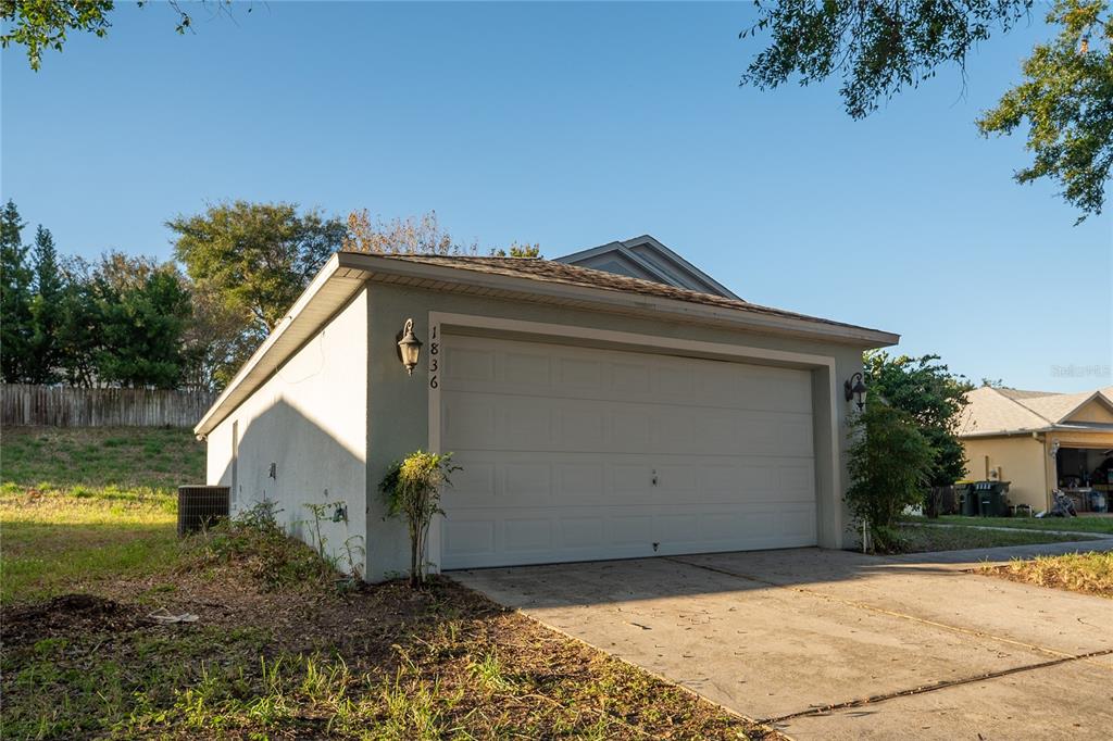 A view of a single-story home's garage exterior with a concrete driveway and surrounding lawn — 1836 RIDGE VALLEY STREET, CLERMONT, FL