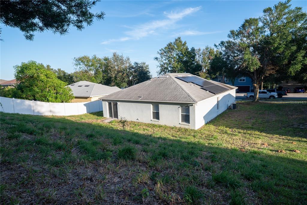 The rear exterior of a single-story house with solar panels and a white vinyl fence — 1836 RIDGE VALLEY STREET, CLERMONT, FL