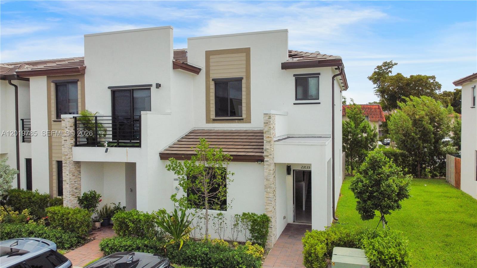 A two-story white stucco townhouse features a balcony, stone accents, and a tiled roof — 21035 NE 8th Ave, Miami FL 33179, MIAMI, FL