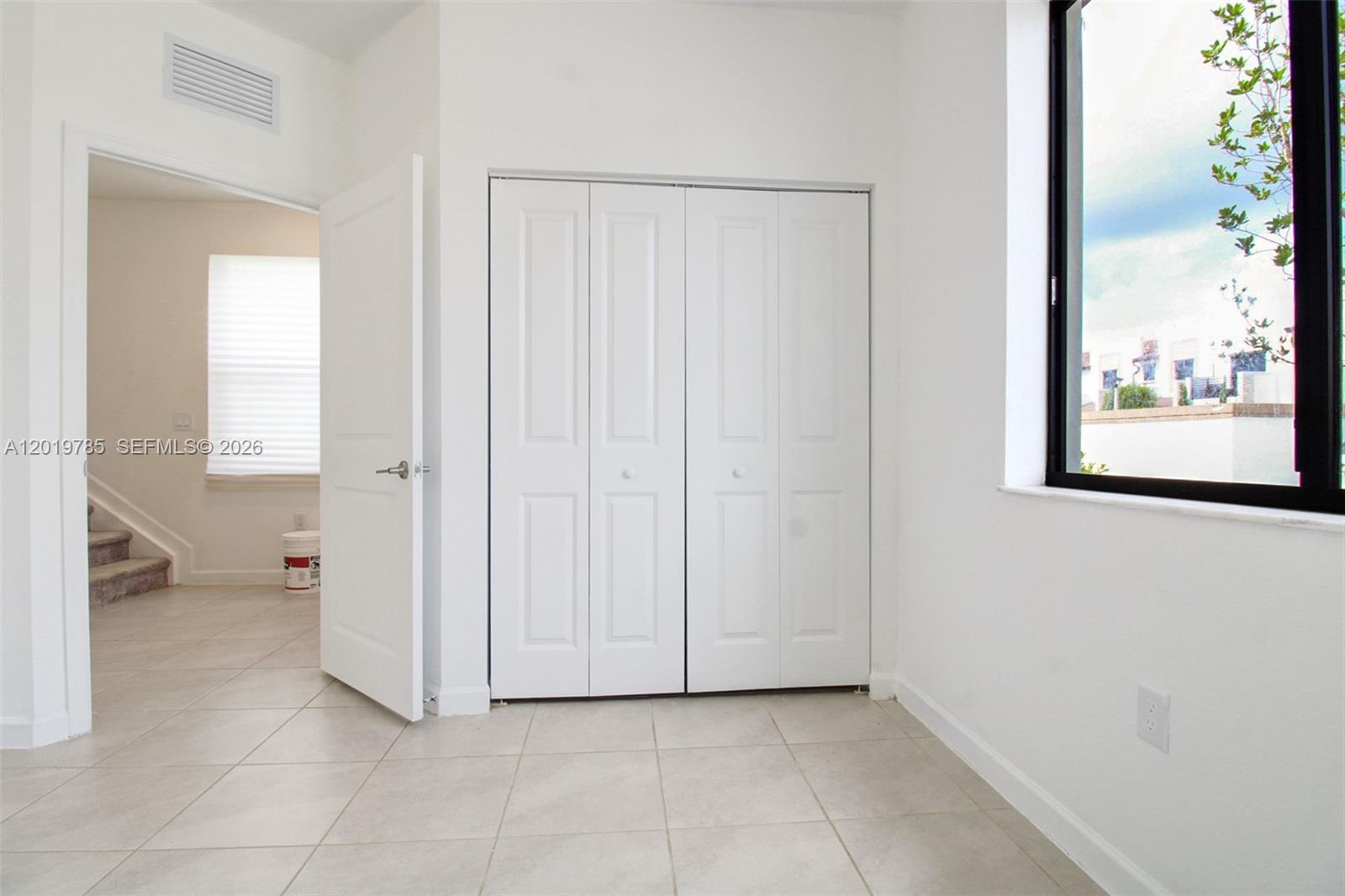 A room with white walls, tile flooring, a closet with bifold doors, and a window — 21035 NE 8th Ave, Miami FL 33179, MIAMI, FL