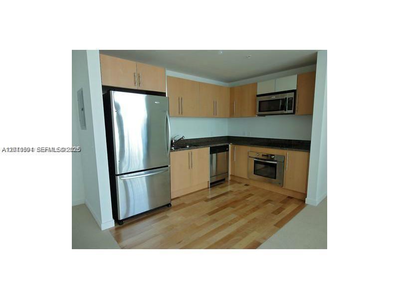 A kitchen features light wood cabinets, stainless steel appliances, and hardwood flooring — 300 S Biscayne Blvd # 2903, Miami FL 33131, MIAMI, FL