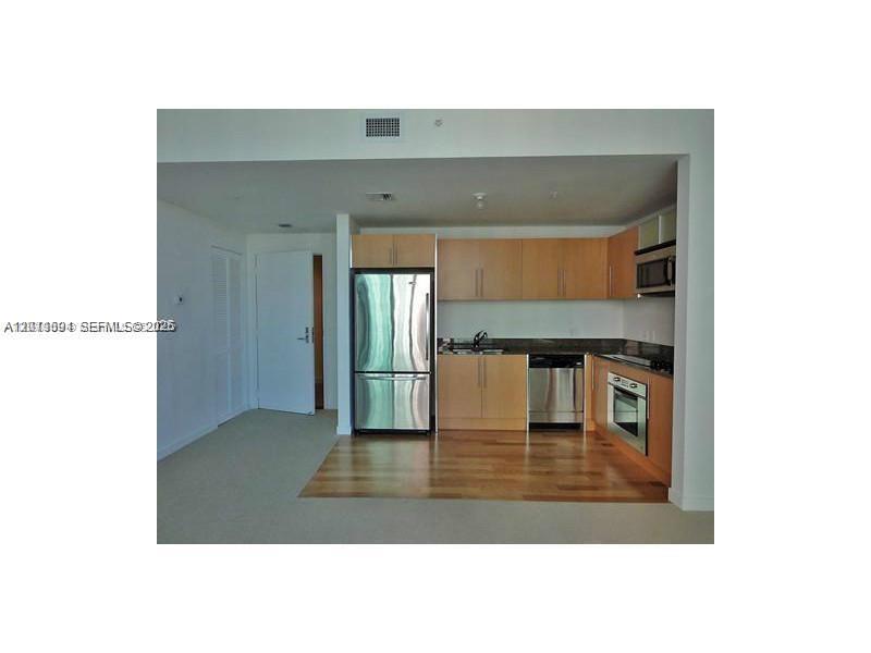 A kitchen features light wood cabinets, stainless steel appliances, and hardwood flooring — 300 S Biscayne Blvd # 2903, Miami FL 33131, MIAMI, FL