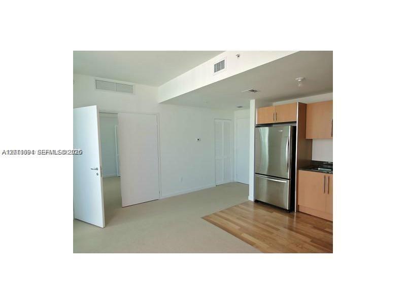 A kitchen with stainless steel appliances and light wood cabinets opens to a carpeted room — 300 S Biscayne Blvd # 2903, Miami FL 33131, MIAMI, FL