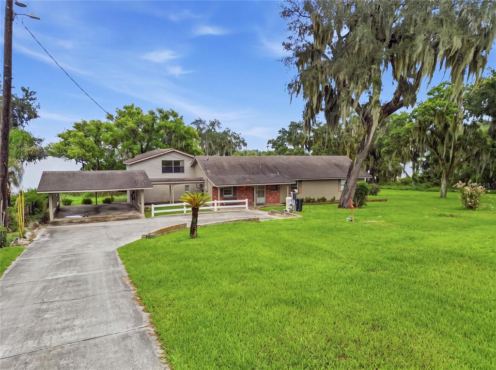 A single-story house with a carport, brick accents, and large trees on a grassy lot — 767 EDISON ROAD, AUBURNDALE, FL