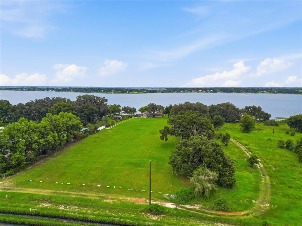 An aerial view shows a large, grassy lot leading to a house beside a lake — 767 EDISON ROAD, AUBURNDALE, FL
