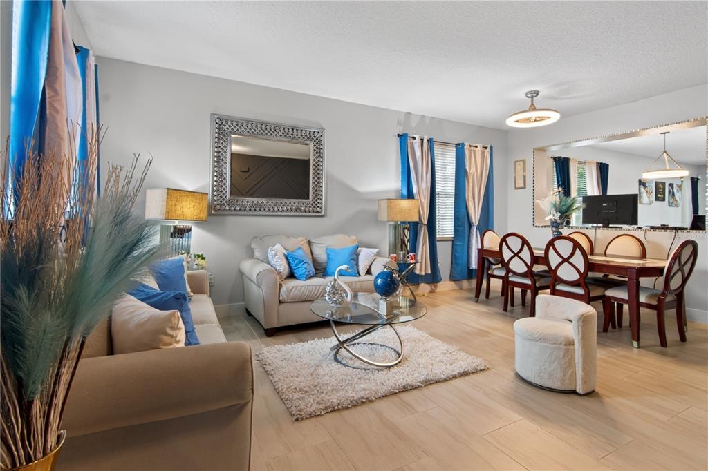 A living and dining room featuring beige sofas, a glass coffee table, and wood-look flooring — 626 BALDWIN DRIVE, KISSIMMEE, FL