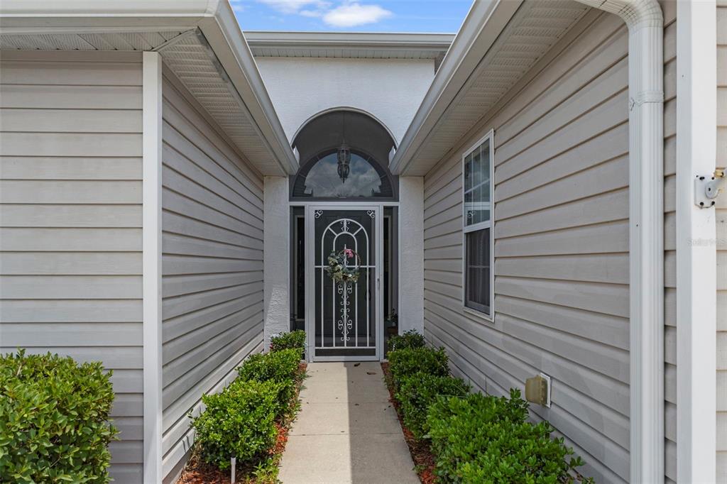 A concrete walkway leads to the front entrance of a house with light-colored vinyl siding — 201 N GOLF HARBOR PATH, INVERNESS, FL