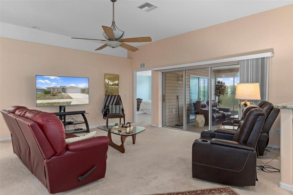 A living room features a red sofa, two brown recliners, a television, and sliding glass doors — 201 N GOLF HARBOR PATH, INVERNESS, FL