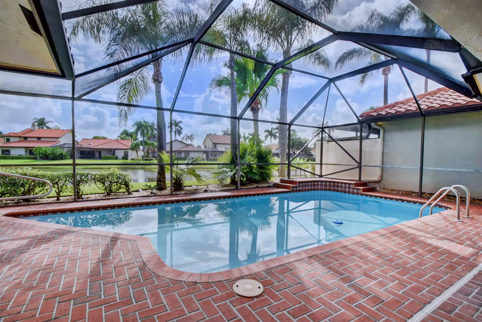 A screened-in swimming pool with a brick deck overlooks a lake and neighboring houses — 22595 Esplanada Circle W, Boca Raton FL 33433, BOCA RATON, FL