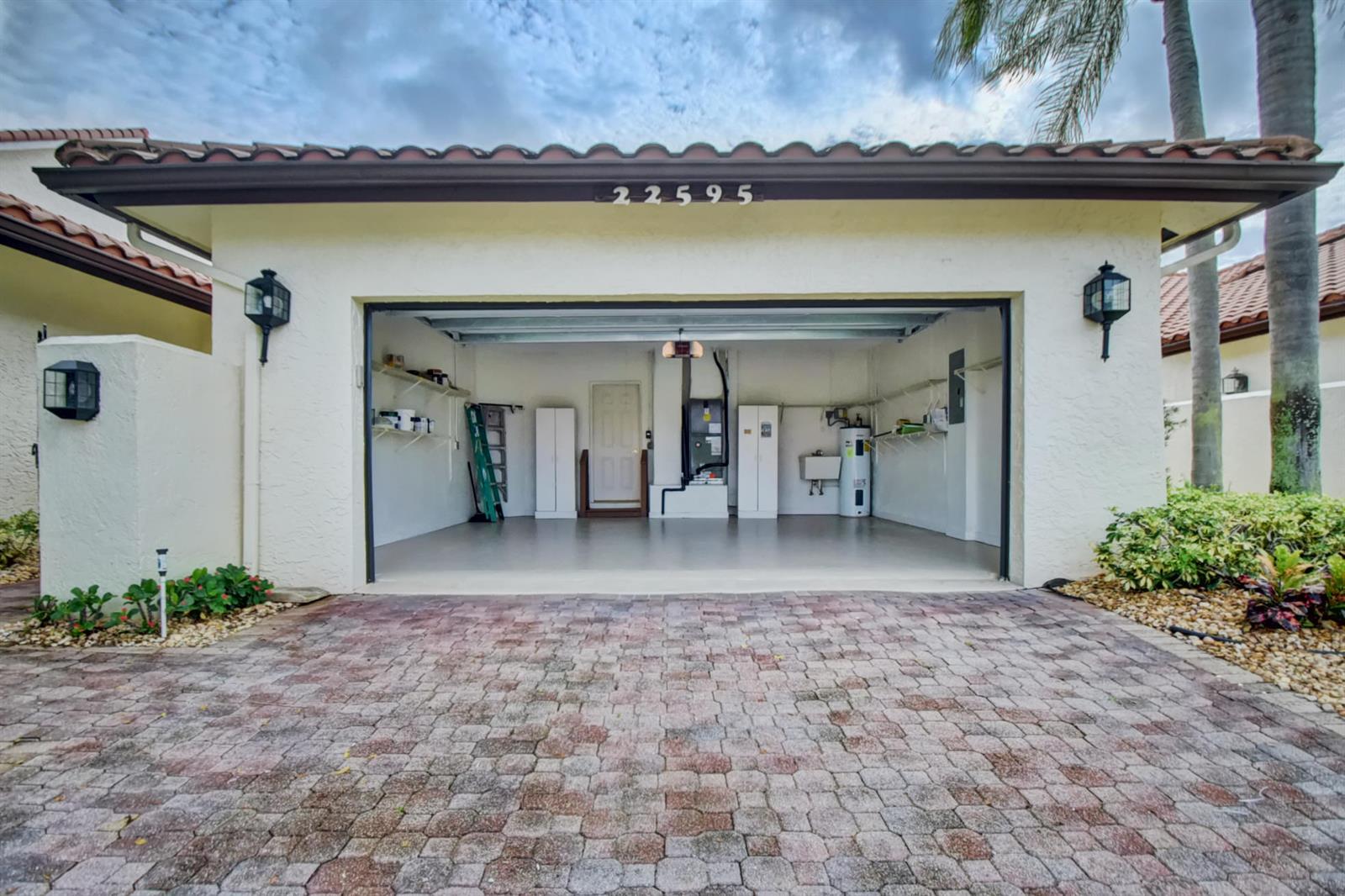 An open garage with a paved driveway, white walls, storage shelving, and utility equipment — 22595 Esplanada Circle W, Boca Raton FL 33433, BOCA RATON, FL