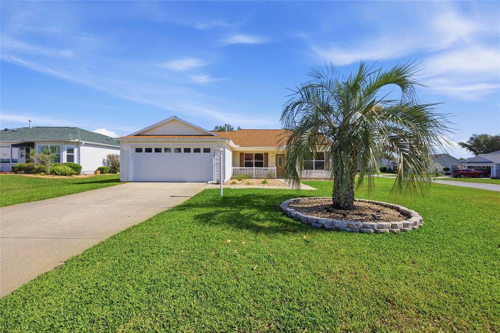 A single-story house with a white garage, tan siding, and a palm tree in the yard — 17705 SE 93RD HAWTHORNE AVENUE, THE VILLAGES, FL