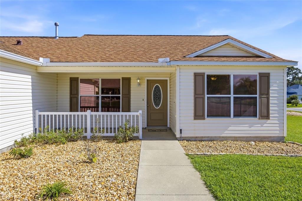 A single-story house with beige siding, a brown shingled roof, and a white front porch — 17705 SE 93RD HAWTHORNE AVENUE, THE VILLAGES, FL
