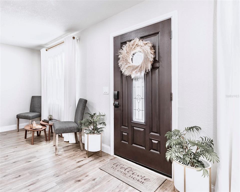 An entryway features a dark brown front door, light wood flooring, and two gray chairs — 6220 INTERBAY, TAMPA, FL