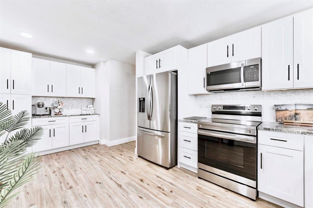 A modern kitchen features white cabinetry, stainless steel appliances, and light wood-look flooring — 6220 INTERBAY, TAMPA, FL