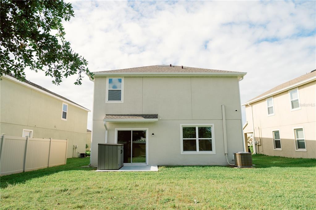 The exterior rear view of a two-story house features a sliding glass door and lawn — 7426 TUSCAN BAY CIRCLE, WESLEY CHAPEL, FL