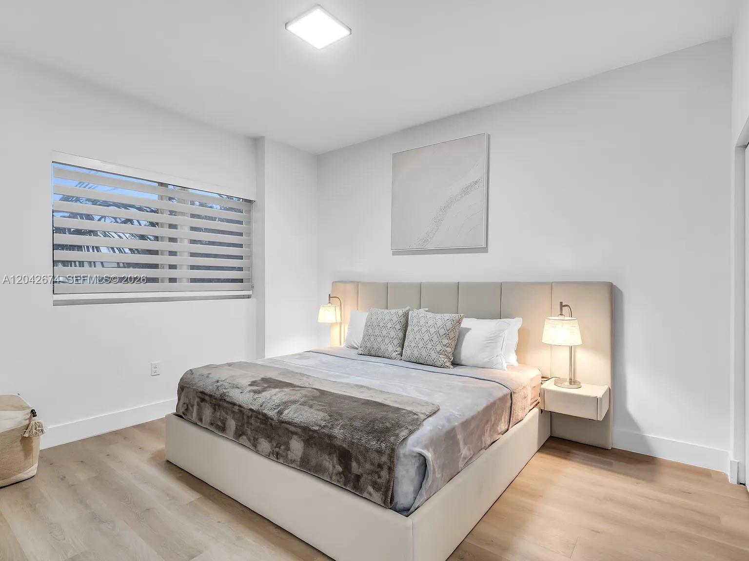 A bedroom features a platform bed with a tall headboard, two lamps, and light flooring — 3728 NW 19th Ave # 305, Miami FL 33142, MIAMI, FL