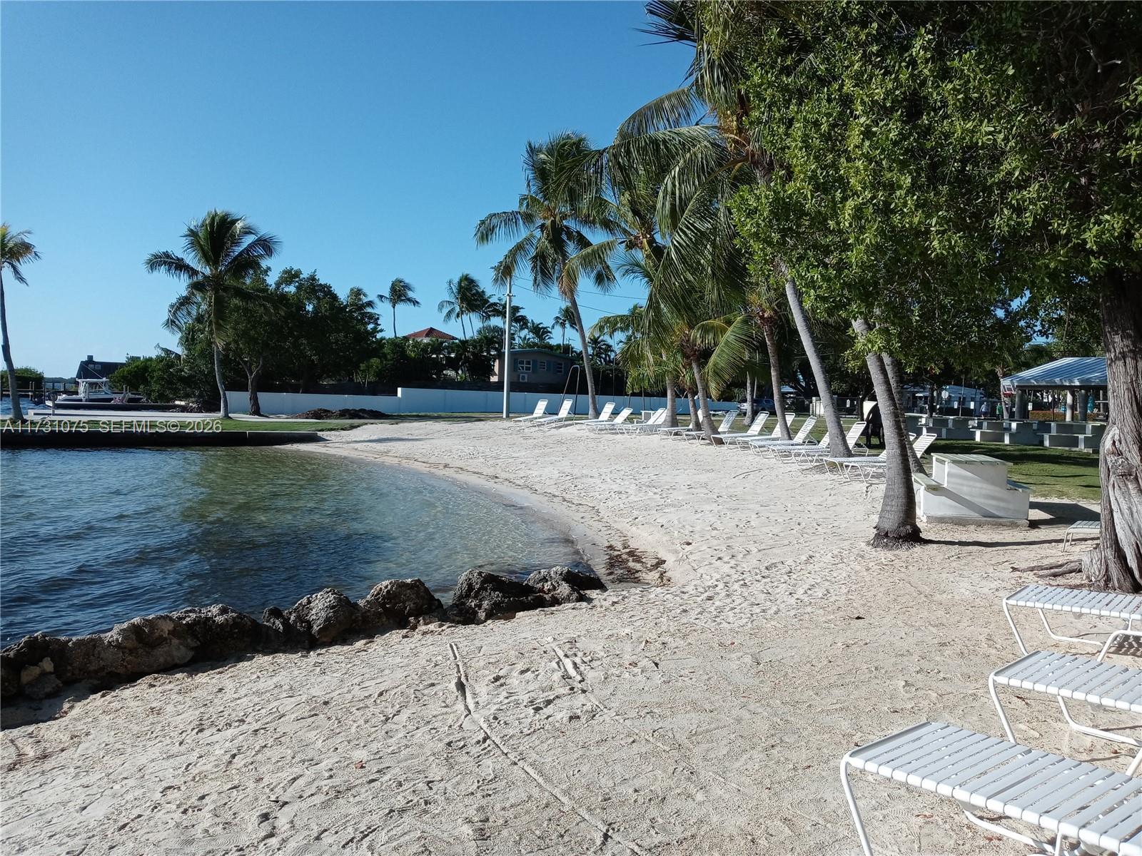 A sandy beach features lounge chairs, palm trees, and a view of the water — 35 Bass Ave., Key Largo FL 33037, KEY LARGO, FL