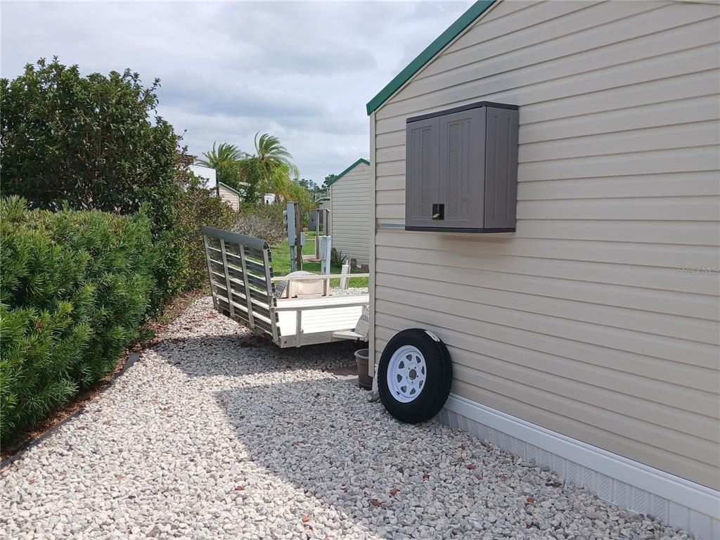 A utility trailer sits on a gravel lot next to a beige vinyl-sided building — 2442 LIMEWOOD AVENUE, CLERMONT, FL