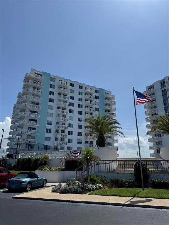 A multi-story apartment building stands behind a parking lot with a blue convertible car — 925 N HALIFAX AVENUE UNIT 102, DAYTONA BEACH, FL