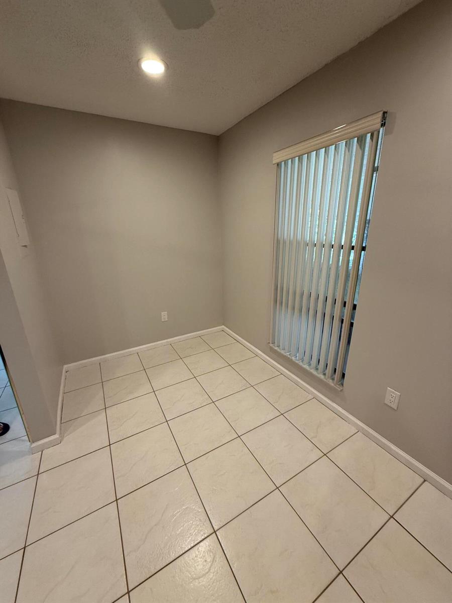 An empty room features light-colored tile flooring, grey walls, and vertical window blinds — 9292 Sabal Ridge Circle # D, Boca Raton FL 33428, BOCA RATON, FL