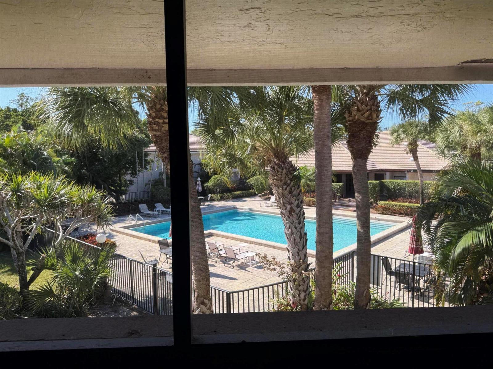 A view from a window overlooking a swimming pool surrounded by palm trees and landscaping — 9292 Sabal Ridge Circle # D, Boca Raton FL 33428, BOCA RATON, FL