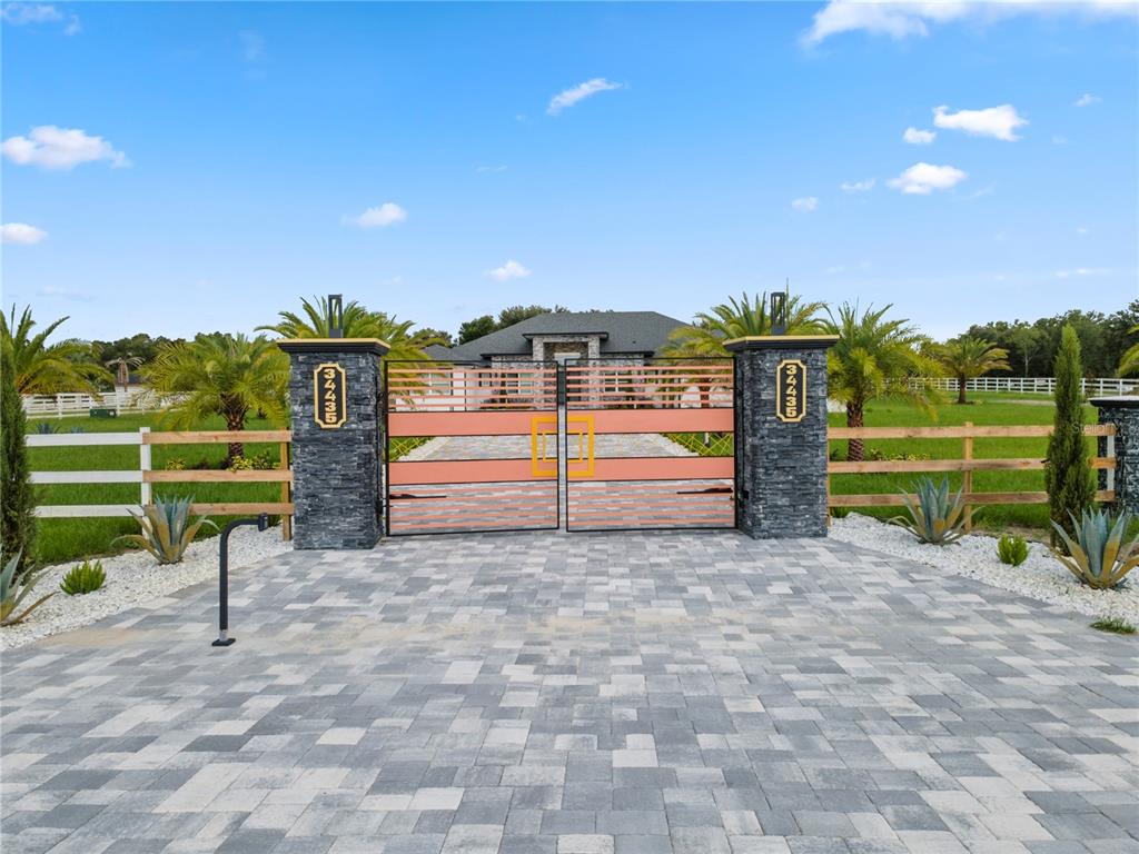 A stone-pillared gate with metal panels opens to a paved driveway leading to a house — 34435 DONNA VISTA PLACE, EUSTIS, FL