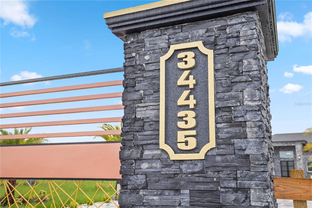 A stone pillar displays a vertical address plaque next to a modern metal gate — 34435 DONNA VISTA PLACE, EUSTIS, FL