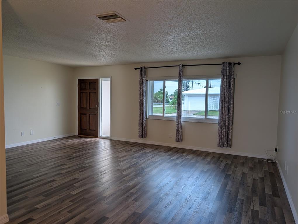 An empty living room features wood-look flooring, a front door, and a large window — 10188 45TH STREET N UNIT 2, PINELLAS PARK, FL